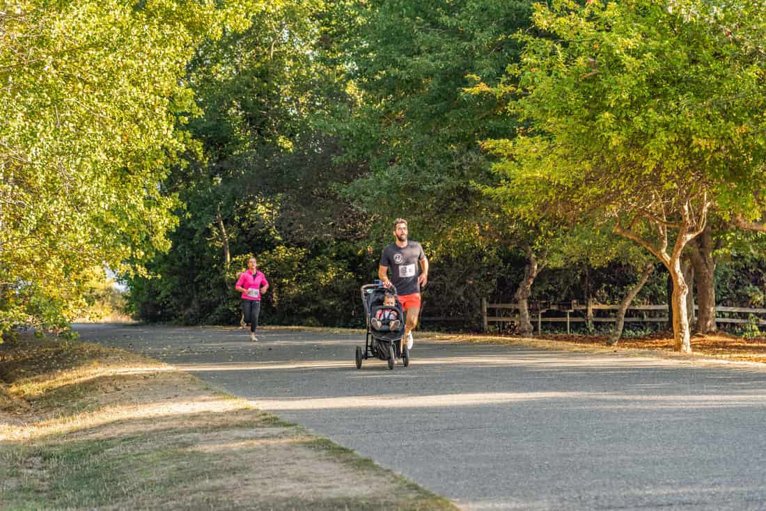 A parent running on a path while pushing a jogging stroller