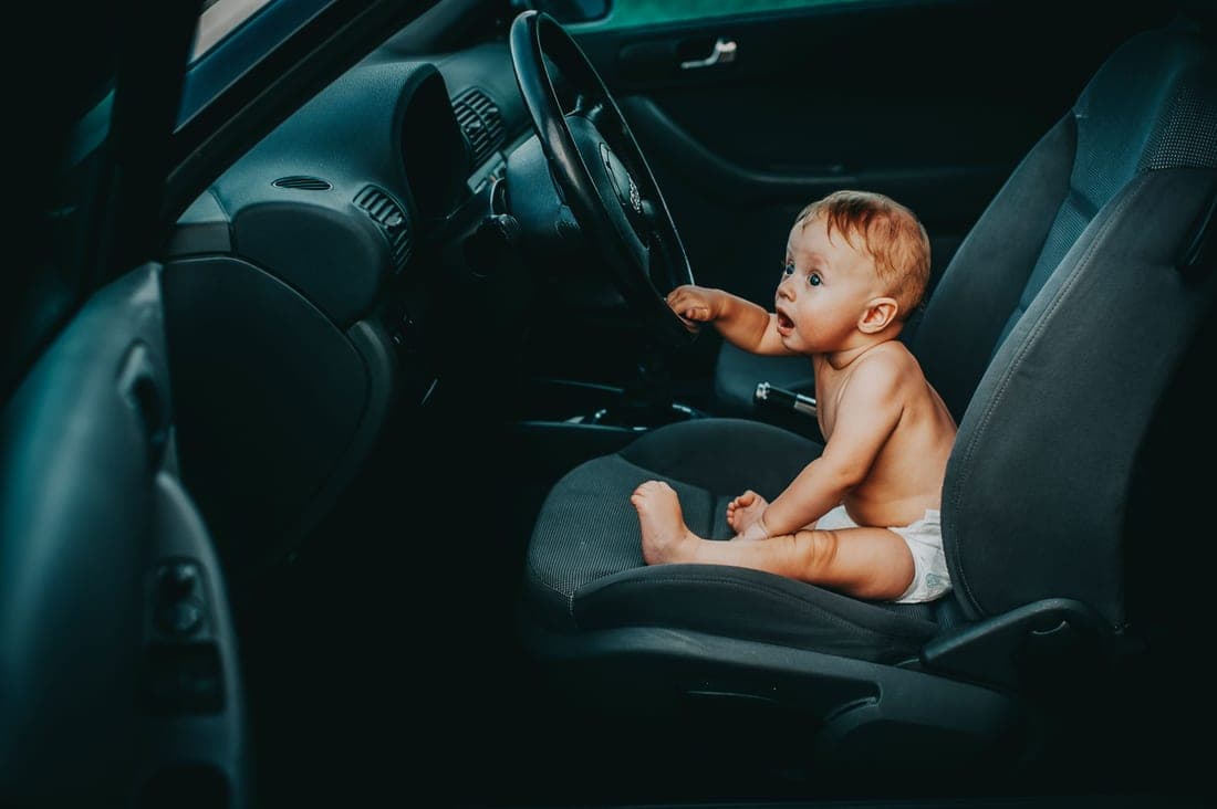 A parent lifting a child into a car seat through an open car door