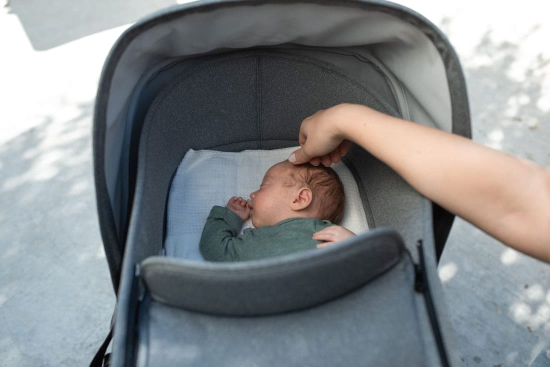 A newborn lying flat in a stroller bassinet outdoors